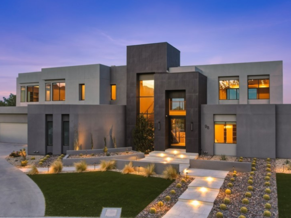 Modern luxury home in The Ridges Las Vegas featuring contemporary architecture, clean geometric lines, desert landscaping, illuminated walkway, and expansive floor-to-ceiling windows at dusk.