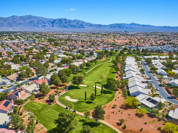 Aerial view of a Las Vegas residential neighborhood with homes surrounding a green golf course and mountains in the background.