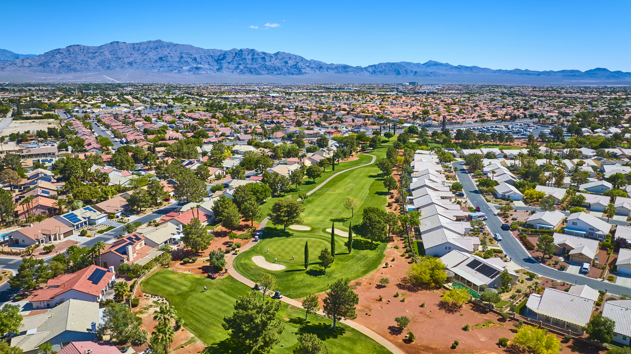 Aerial view of a Las Vegas residential neighborhood with homes surrounding a green golf course and mountains in the background.