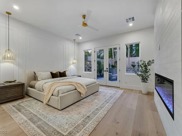 Contemporary primary bedroom with light wood floors, vaulted ceiling, pendant lighting, modern fireplace and French doors opening to a private patio.